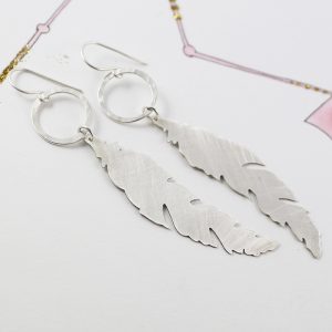 Hand pierced sterling silver feather hanging on a beautiful hammered silver hoop by chloe michell jewellery
